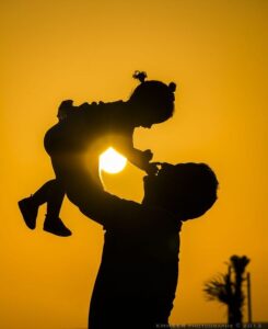 Father lifting child against sunset